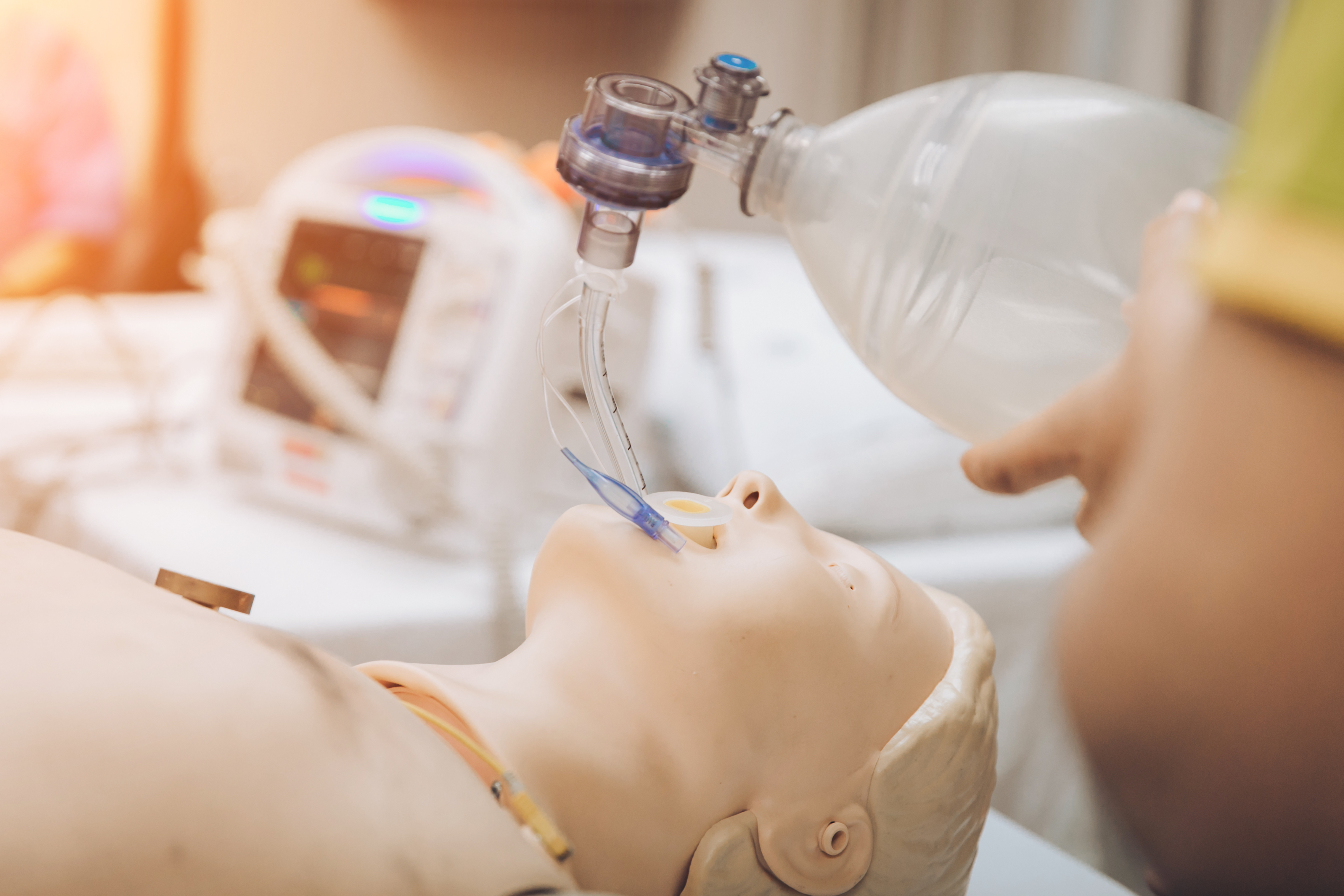 A person using a bag-valve-mask medical device on a dummy patient to practice intubation.