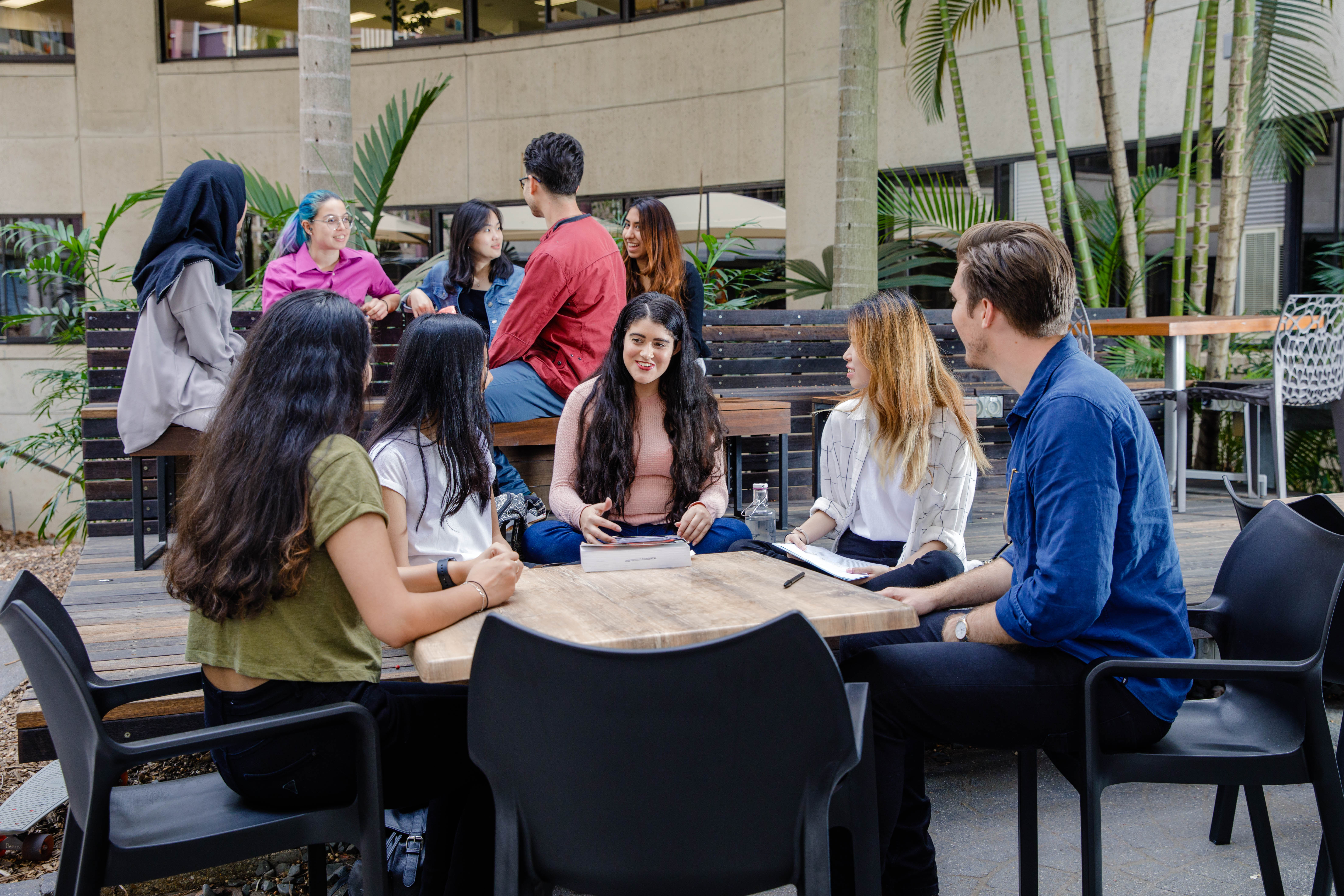 A group of people sitting around a table outside having a discussion. 