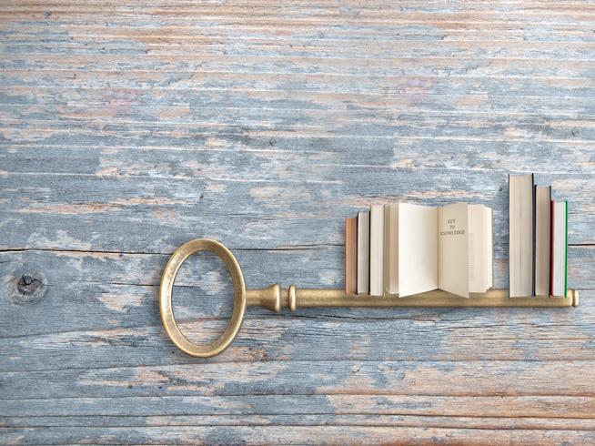 A key with teeth shaped like books on a wooden table.