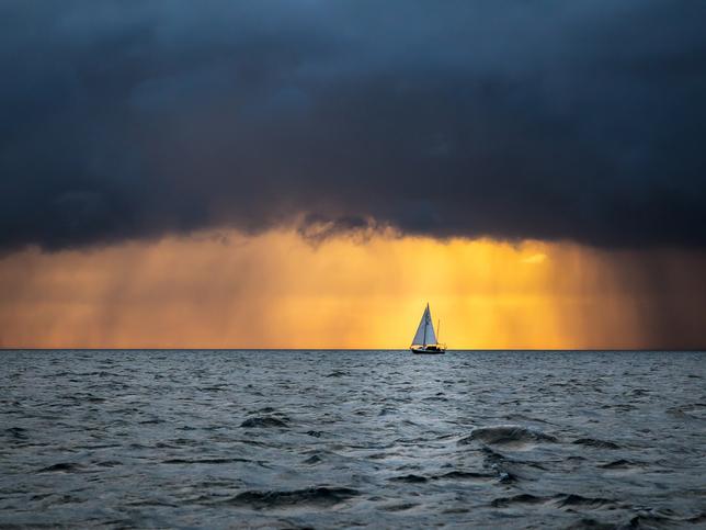 A sailboat in the ocean with dark clouds heavy with rain.