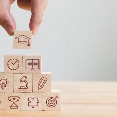 A hand placing a block on top of a stack of wooden blocks. Each block has a icon image related to learning.