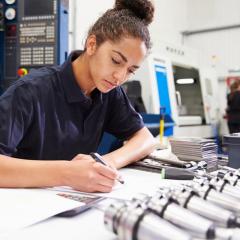 Engineering student sitting at desk in lab and writing on a piece of paper.