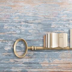 A key with teeth shaped like books on a wooden table.