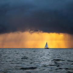 A sailboat in the ocean with dark clouds heavy with rain.